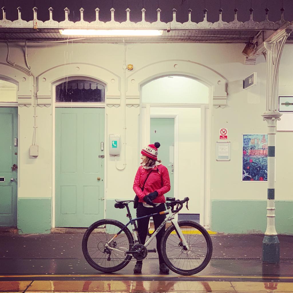 Looking from behind at young lady on bike stopping to admire coastal view from high vantage point